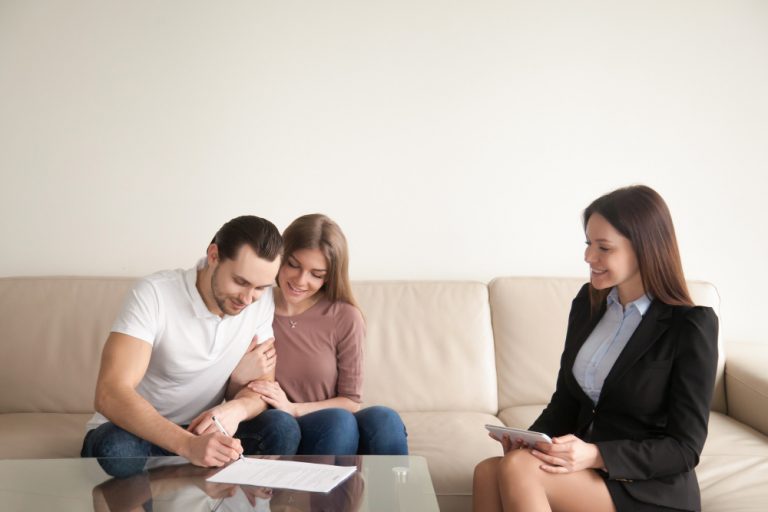 young man signing papers sitting wife realtor
